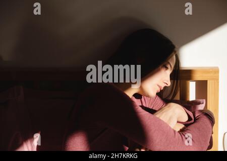 Besorgte junge Frau, die zu Hause auf dem Bett sitzt Stockfoto