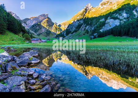 Berge spiegeln sich im klaren Wasser des Seepsees bei Sonnenaufgang mit einsamen Hütten im Hintergrund Stockfoto