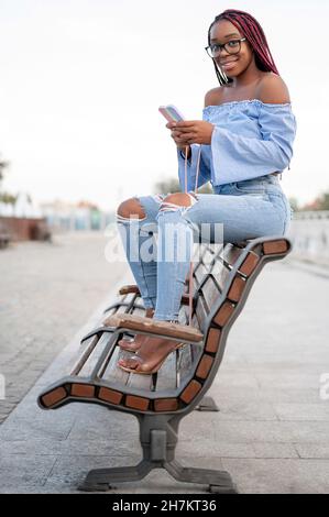 Lächelnde Frau mit Mobiltelefon auf der Bank Stockfoto