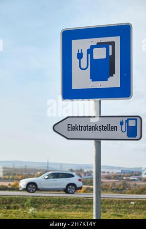 Elektrofahrzeug Ladestation Schild mit Auto vorbei im Hintergrund Stockfoto