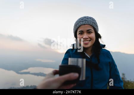 Lächelnde junge Frau beim Sonnenuntergang mit Kaffeebecher mit Freundin toasten Stockfoto