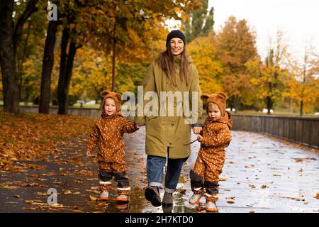 Lächelnde Mutter hält Zwillingshände im Herbstpark Stockfoto