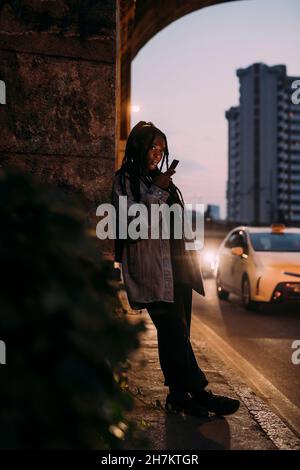 Frau, die nachts das Mobiltelefon auf dem Fußweg hält Stockfoto