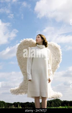 Teenager-Mädchen mit weißen Flügeln, die an einem sonnigen Tag nachsinnen Stockfoto