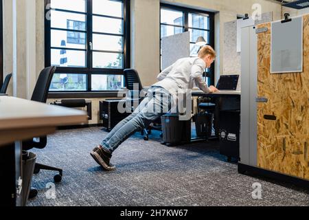 Junger Geschäftsmann, der Liegestütze am Arbeitsplatz macht Stockfoto