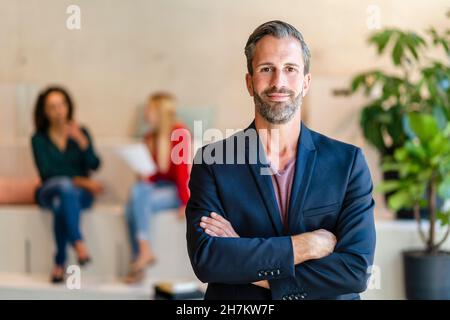 Lächelnder bärtiger Geschäftsmann mit gekreuzten Armen im Büro Stockfoto