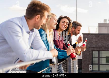 Kollegen trinken, während sie sich auf das Geländer der Terrasse lehnen Stockfoto