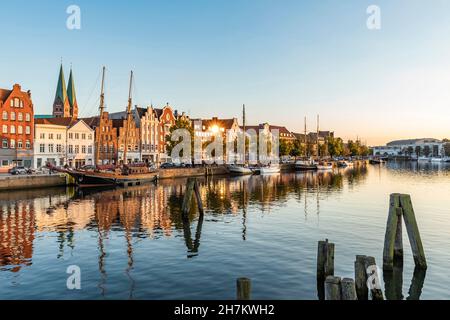 Deutschland, Schleswig-Holstein, Lübeck, in der Abenddämmerung liegen Schiffe am Trave-Kanal mit historischen Stadthäusern im Hintergrund Stockfoto