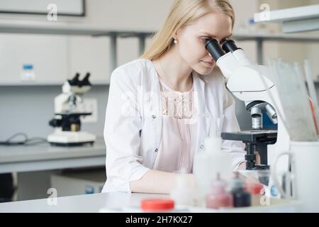 Blonde Wissenschaftlerin, die im Labor mikroskopisch forscht Stockfoto