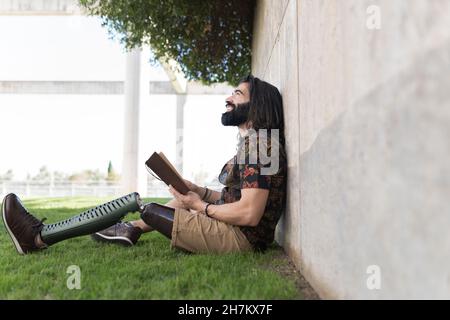 Lächelnder Mann mit künstlichen Gliedmaßen, der im Park ein Buch liest Stockfoto