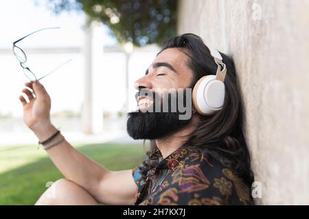 Bärtiger Mann mit geschlossenen Augen, der im öffentlichen Park Musik hört Stockfoto