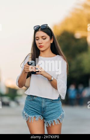 Junge Frau in Denim-Shorts mit Smartphone Stockfoto