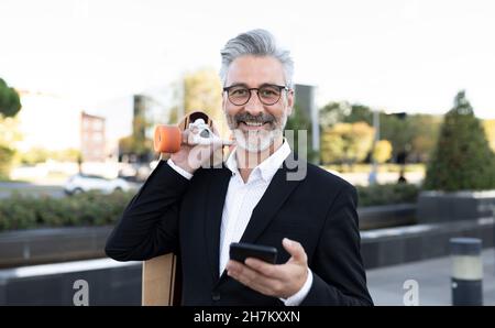Geschäftsmann mit Smartphone und Skateboard Stockfoto
