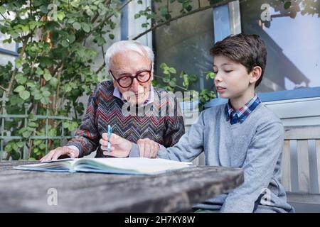 Großvater unterstützt Jungen beim Studieren im Hinterhof Stockfoto