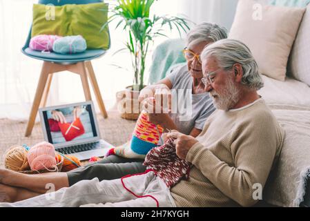 Ältere Frau lehrt den Mann, zu Hause Wolle mit Nadel zu stricken Stockfoto