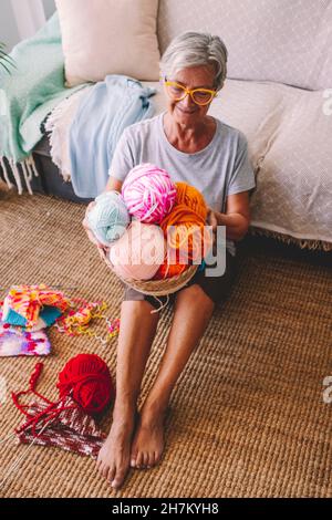 Frau mit Korb aus Wollkugeln im Wohnzimmer sitzen Stockfoto