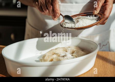 Frau, die zu Hause geriebene Kokosnuss auf den Teig in die Schüssel legt Stockfoto