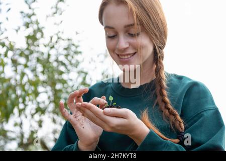 Lächelnde Farmerin mit geflochtenen Haaren, die die Pflanze in der Hand berühren Stockfoto