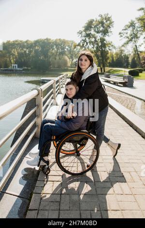 Frau umarmt Mann, der im Rollstuhl am Damm sitzt Stockfoto