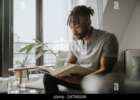 Junger bärtiger Mann liest Buch auf dem Sofa Stockfoto