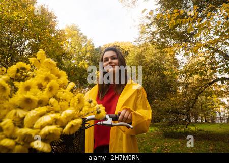 Lächelnde Frau mit gelben Blumen auf dem Fahrrad im Park Stockfoto