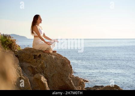 Sportlerin meditiert in Lotusposition auf Felsen bei Sonnenuntergang Stockfoto