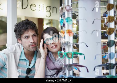 Frau versucht auf Brillen von Freund im Geschäft Stockfoto