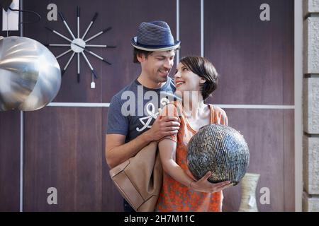 Lächelnder Mann, der die Freundin ansieht, die die Vase im Laden hält Stockfoto