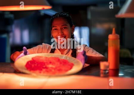 Lächelnde Küchenhelferin zeigt Carpacio auf dem Teller Stockfoto