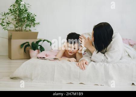 Mutter im Gespräch mit Sohn, der im neuen Haus auf dem Bett liegt Stockfoto