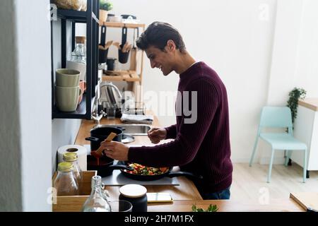 Junger Mann, der zu Hause in der Küche Essen zubereitet Stockfoto
