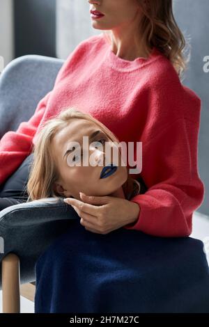 Junge Frau, die sich von der Zwillingsschwester auf einem Stuhl lehnt Stockfoto