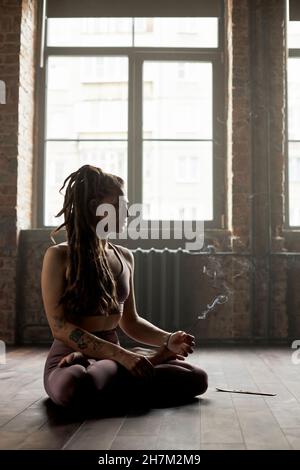 Sportlerin mit Räucherstäbchen meditiert im Yoga-Studio Stockfoto