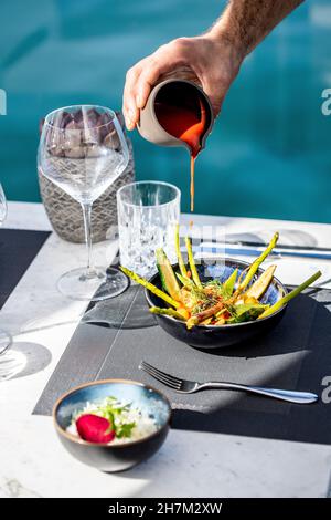 Der Koch gießt Sauce auf den Salat am Tisch Stockfoto