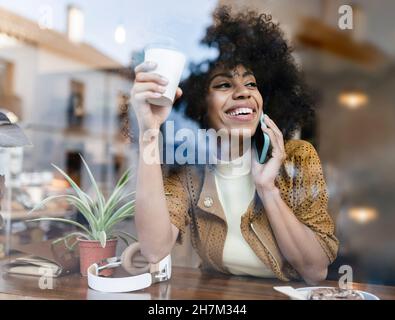 Lächelnde Frau mit Einweg-Kaffeetasse, die aus dem Fenster schaute Stockfoto