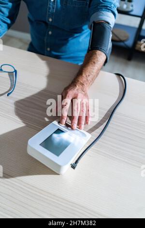 Älterer Mann, der zu Hause ein Blutdruckmessgerät verwendet Stockfoto