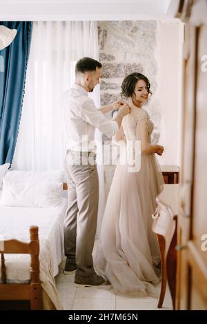 Der Bräutigam schließt die Knöpfe am Brautkleid Stockfoto