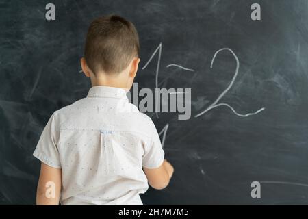 Rückansicht eines Schülers in einer Klasse schreibt Kreidenummern auf eine Tafel. Matheunterricht. Junior School. Bildungskonzept. Zurück zur Schule. Für Text platzieren. Stockfoto