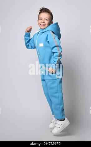 Frolic, Active Kid Boy in blauem Jumpsuit mit Kapuze, Taschen und reflektierenden Streifen hat Spaß beim Springen, Lachen. Seitenansicht Stockfoto