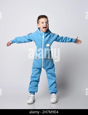 Frolic Kid Boy in blauem Jumpsuit mit Reißverschluss und Taschen steht weit auseinander und schreit laut Stockfoto