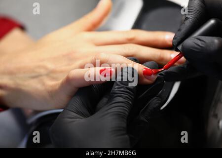 Professionelle Salonarbeiter decken Kunden Nägel mit roter Farbpolitur ab Stockfoto