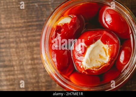 Gefüllte Kirschpaprika mit Ricotta-Käsefüllung im Glas auf Holzboden Stockfoto