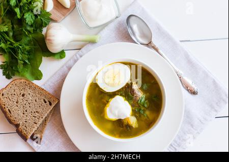 Gesunde grüne Suppe aus Sauerampfer und Brennnessel mit gekochtem Ei und Sauerrahm in einer weißen Schüssel. Traditionelle russische Küche. Draufsicht Stockfoto
