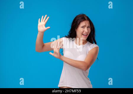 Studioportrait einer jungen schönen Frau in einem weißen T-Shirt vor einem blauen Wandhintergrund. Menschen aufrichtige Emotionen. Stockfoto