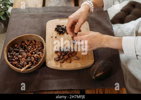 Hände schälen Bio-Kakaobohnen auf Holztisch, Kakaobohnen, handwerkliche Schokolade in rustikalem Stil für die Zeremonie auf dem Tisch. Degustation Stockfoto