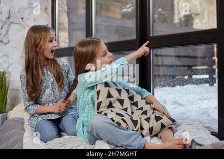 Das Bild von zwei kleinen Schwestern, die auf dem Fensterbrett sitzen und auf das Fenster schauen Stockfoto