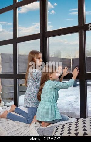 Das Bild von zwei kleinen Schwestern, die auf dem Fensterbrett sitzen und auf das Fenster schauen Stockfoto