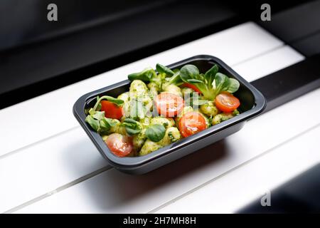 Basilikum Gnocchi mit Tomaten und Salat. Box-Diät, appetitliches Mittagessen zum Mitnehmen. Appetitliches Fertiggericht in einer Einwegbox. Kulinarische Photogrammetrie Stockfoto