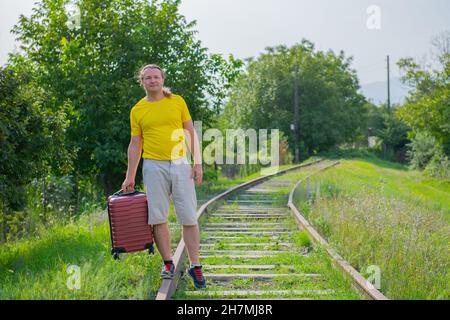 Glücklicher Reisender mit einem Koffer auf den Schienen geht Stockfoto