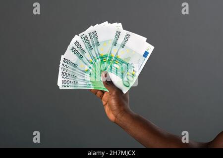 Schwarze Hand mit großem Fächer von 100-Euro-Banknoten und einem Studiohintergrund. Stockfoto